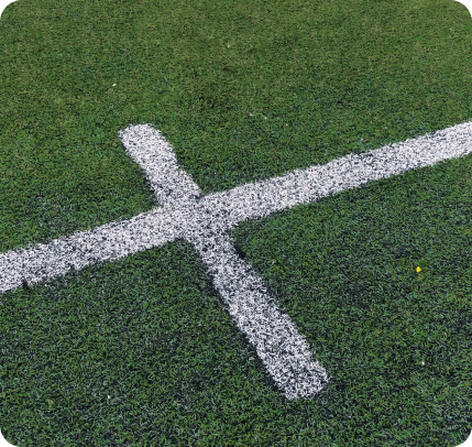 Une ligne blanche croisée est peinte sur un terrain de sport en herbe verte.