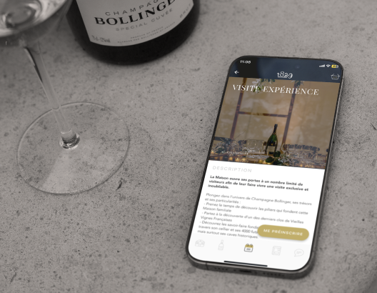 Un smartphone affiche des informations sur une visite d'expérience, posé sur une table en béton à côté d'un verre et d'une bouteille de Champagne Bollinger. Texte à l'écran: VISITE EXPERIENCE
DESCRIPTION
La Maison ouvre ses portes à un nombre limité de visiteurs afin de faire vivre une visite exclusive et mémorable.
Plongez dans l’univers de Champagne Bollinger, ses secrets de fabrication, et ses savoir-faire.
- Visites privées menées par des guides fondateurs et histo...
Meilleur Accueil de France dans la vallée depuis 2001.